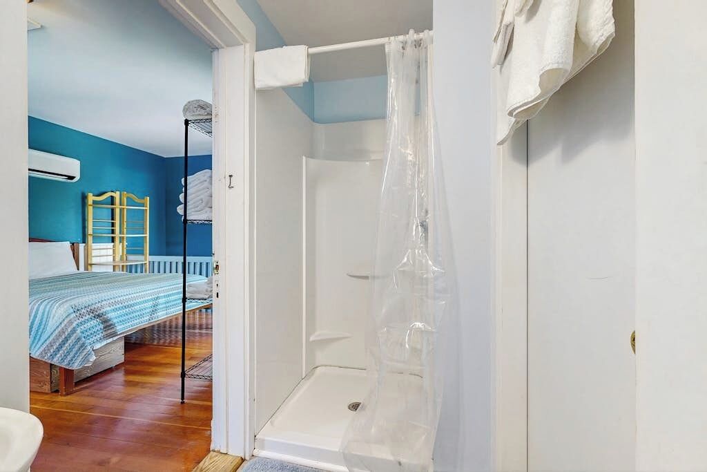 A bathroom with a shower, a bed with a blue and white striped bedspread, and a wooden headboard.