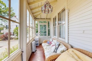 A covered porch with a wicker sofa, a radiator, and a door leading outside. - Dog-friendly House With Wifi and Deck - Near the Water, Eateries, and Shopping (Bar Harbor)