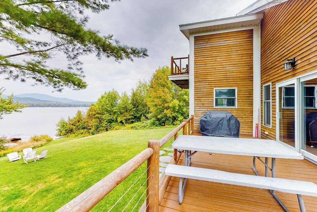 A wooden deck with a picnic table and chairs overlooking a lake.