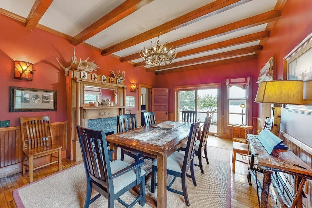 Ein rustikaler Speisesaal mit Holztisch und -stühlen, einer Chandelier und einem Kamin mit Geweihdekorationen.