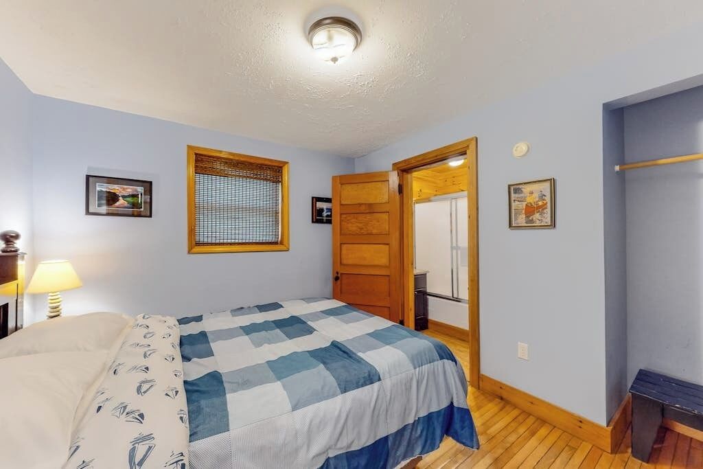 Une chambre à coucher avec un lit, une fenêtre avec des stores, une porte et un luminaire fixé au mur.