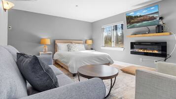 A modern bedroom with a bed, a TV mounted on the wall, a fireplace, and a window.