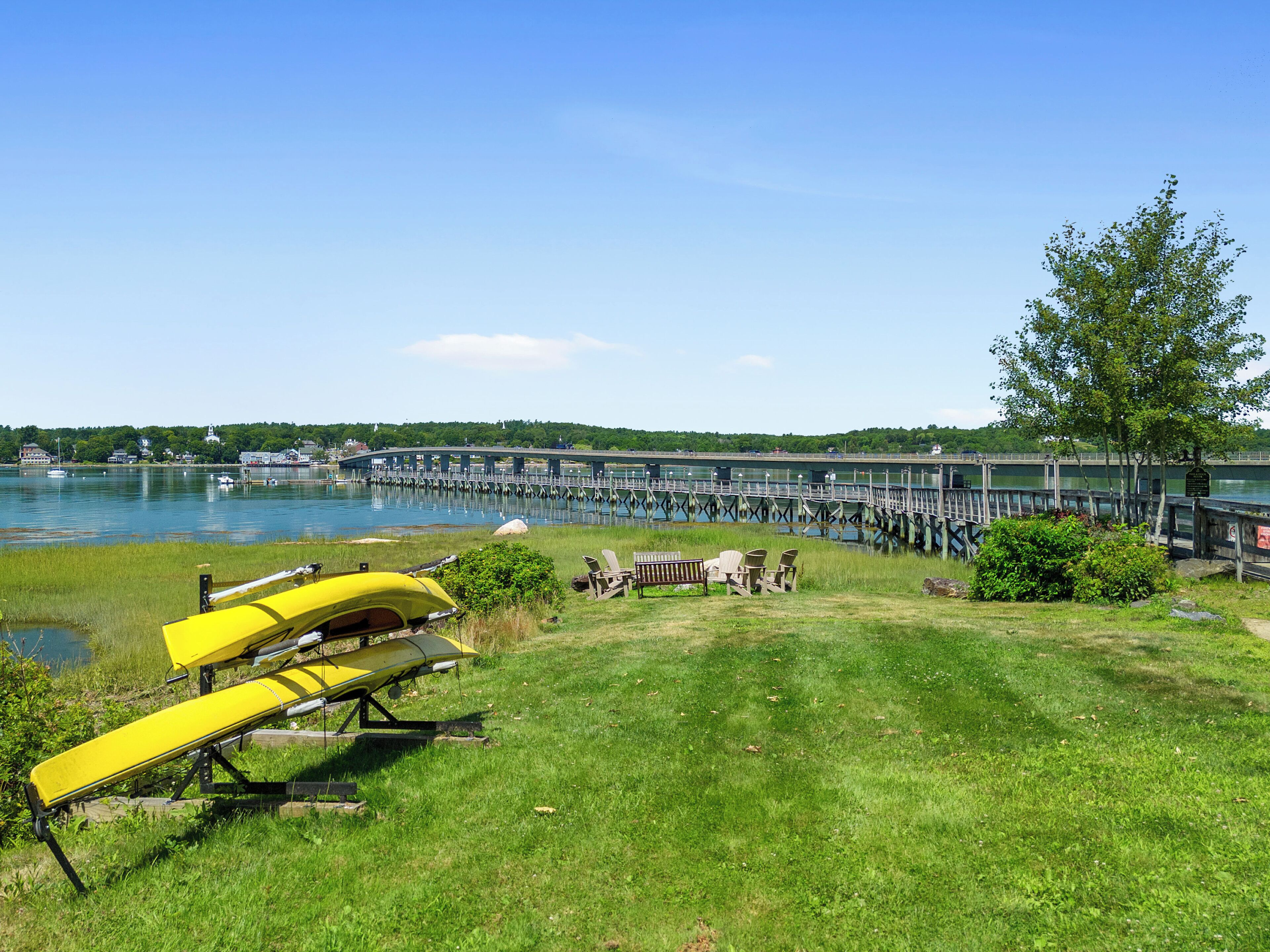 A grassy area with a yellow kayak, a bench, and a tree.