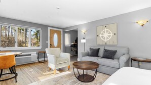 Ein modernes Wohnzimmer mit einem grauen Sofa, einem runden Couchtisch aus Holz und einem weißen Bett.