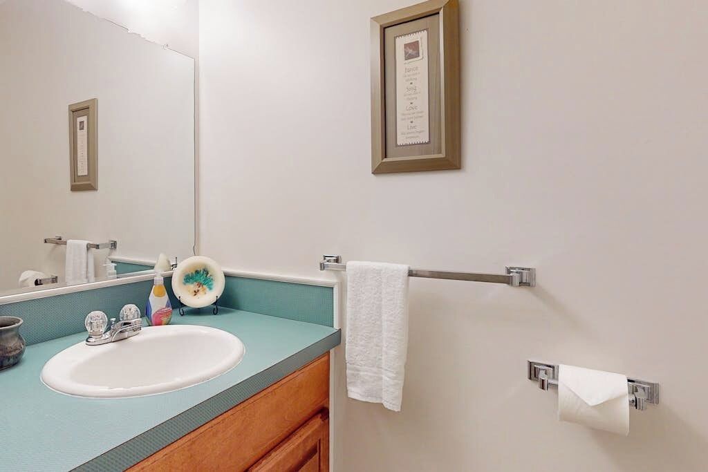 A bathroom with a sink, mirror, towel rack, and a framed quote on the wall.