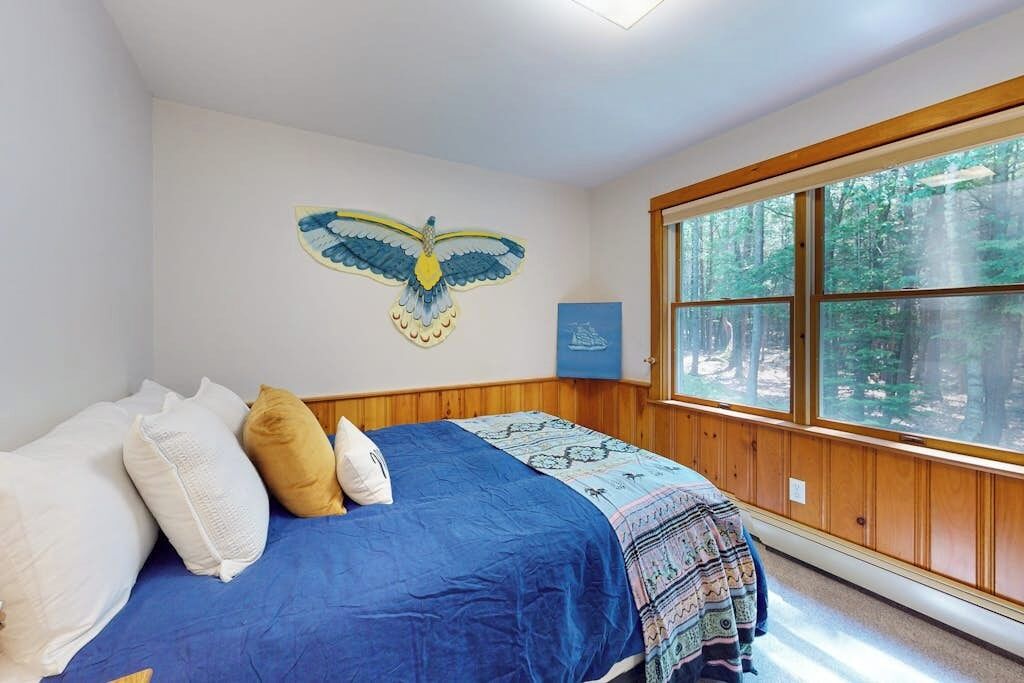 A bedroom with a large window, a bed with blue bedding, and a wall-mounted owl artwork.
