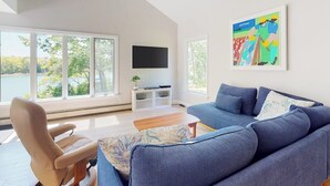 Un soggiorno moderno con una grande finestra, un divano blu, una poltrona beige, un televisore piatto e un quadro colorato.