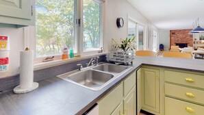 Una cucina con un lavello doppio, mobili verdi e una finestra vista alberi.