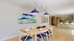 Zona pranzo con tavolo in legno, sedie bianche e lampade a sospensione blu.