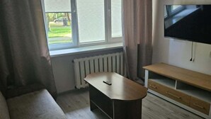 A living room with a sofa, a coffee table, a TV, and a window with curtains. - Beautiful 1-bedroom apartment in charming Liepāja perfect for relaxing stay (Liepāja)