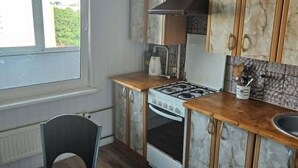 A kitchen with a stove, oven, and cabinets, a dining table with chairs, and a window with curtains. - Beautiful 1-bedroom apartment in charming Liepāja perfect for relaxing stay (Liepāja)