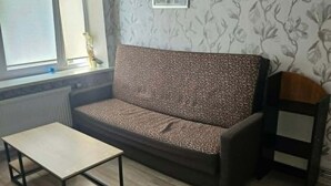 A living room with a sofa, a coffee table, a small side table, a window, and a wall with a floral pattern. - Beautiful 1-bedroom apartment in charming Liepāja perfect for relaxing stay (Liepāja)