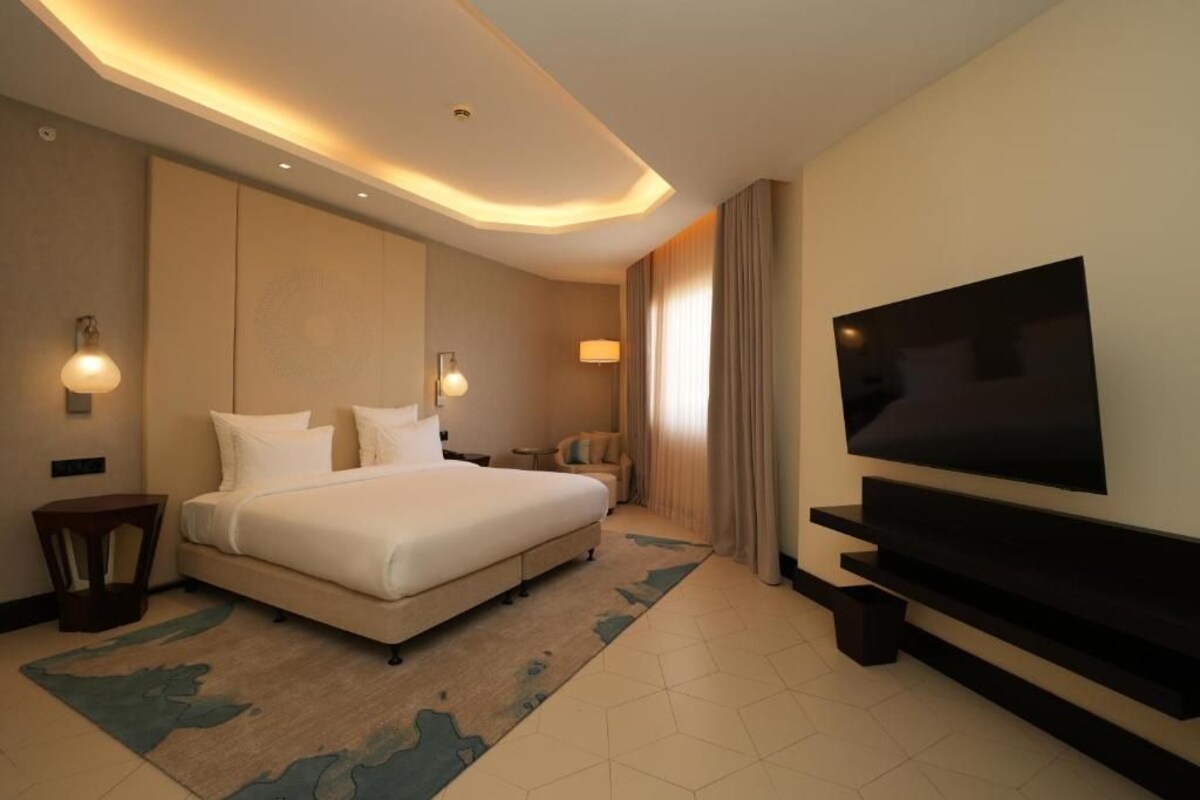 Una habitación de hotel con una cama grande, un televisor de pantalla plana y una mesita auxiliar.