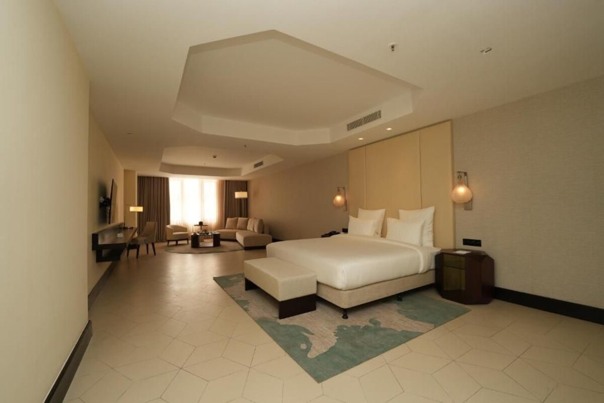 Una habitación de hotel con una cama grande, una zona de estar con un sofá y sillones, un escritorio y un televisor.