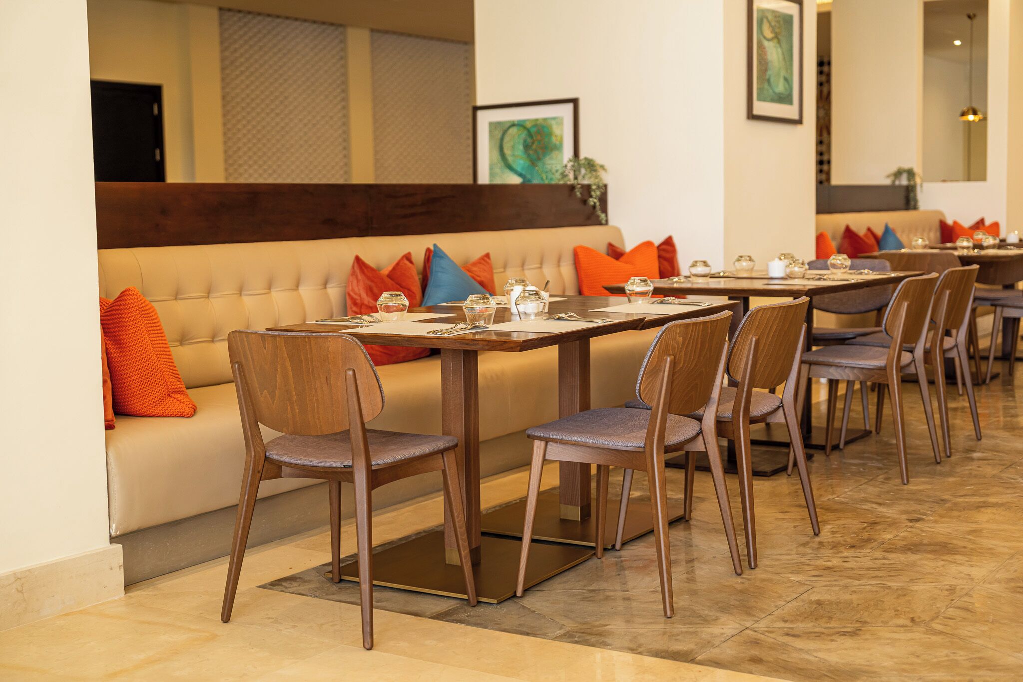 A dining area with a long table, multiple chairs, and a sofa with colorful cushions.