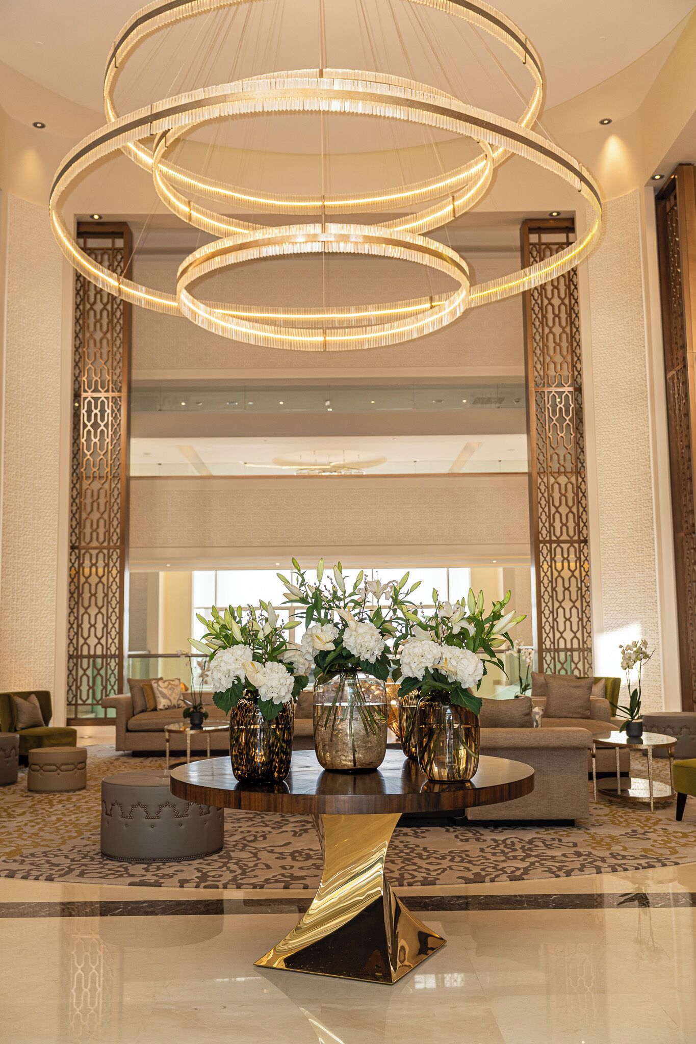 Un hall d’entrée spacieux, agrémenté d’un grand lustre, d’un coin salon et de vases décoratifs remplis de fleurs.