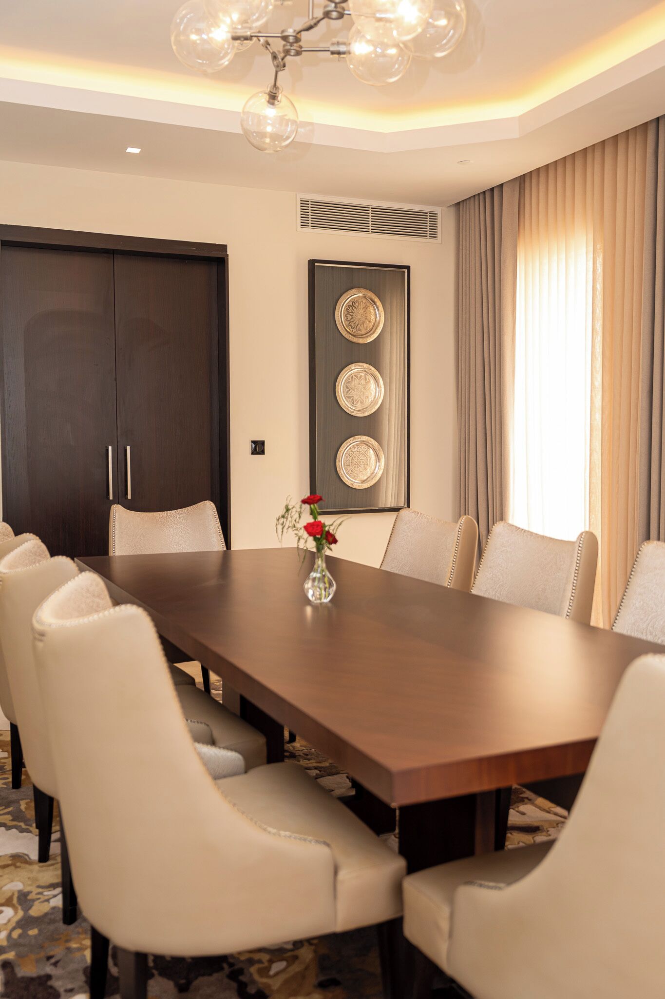 A conference room with a long table, six chairs, a vase with flowers, and decorative plates on the wall.