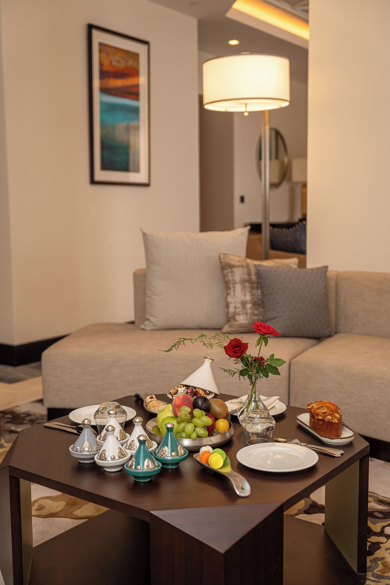 Et hyggeligt opholdsrum med sofa, sofabord med mad og drikke, samt en lampe.