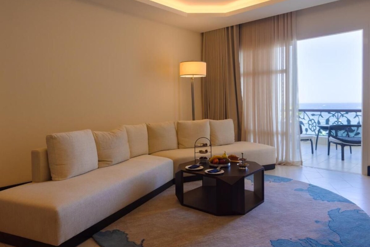 Una habitación de hotel moderna con sofá, una mesa de centro con fruta, una lámpara y vista al mar.