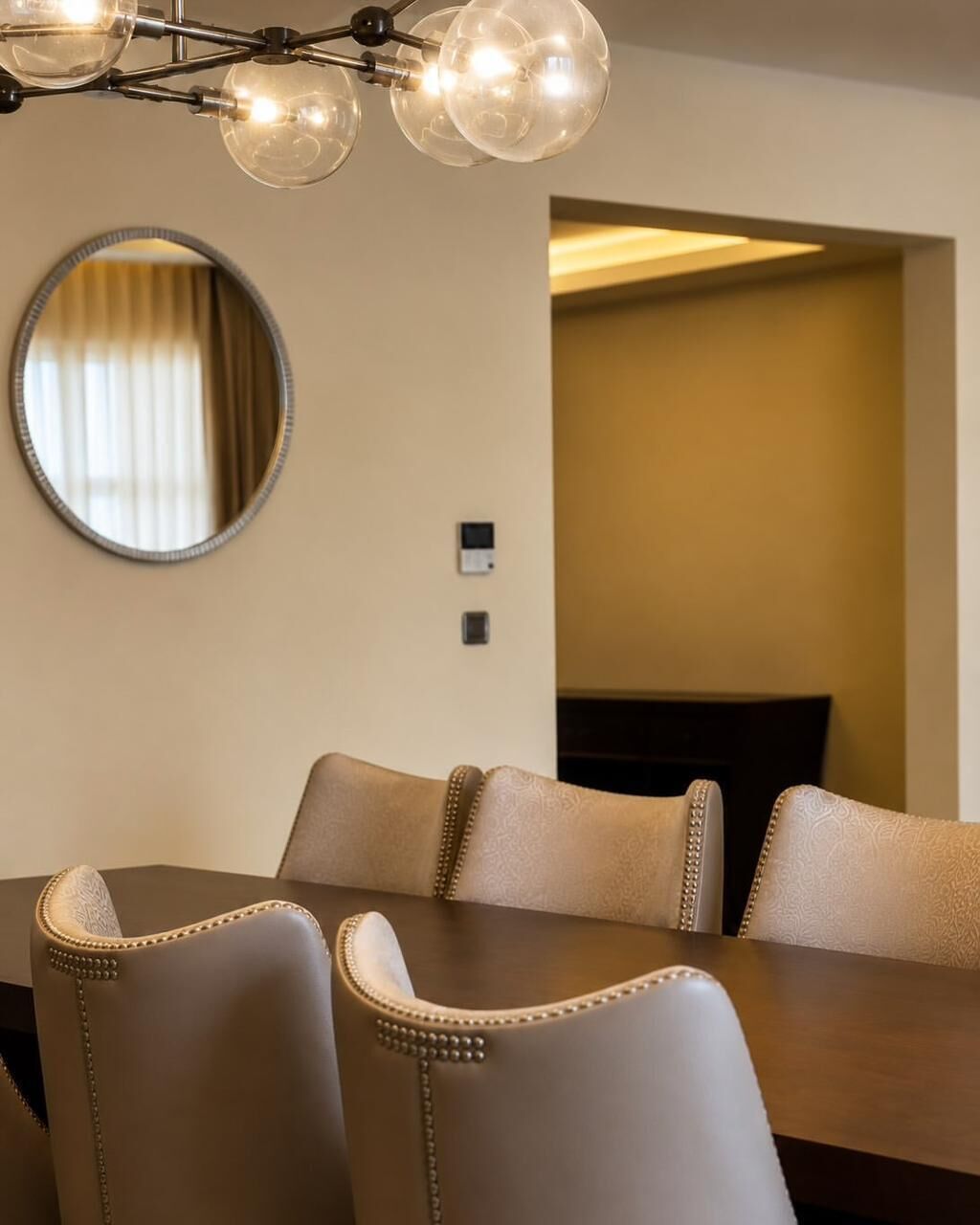 Un coin repas avec une table et des chaises en bois, un miroir rond et un lustre moderne.