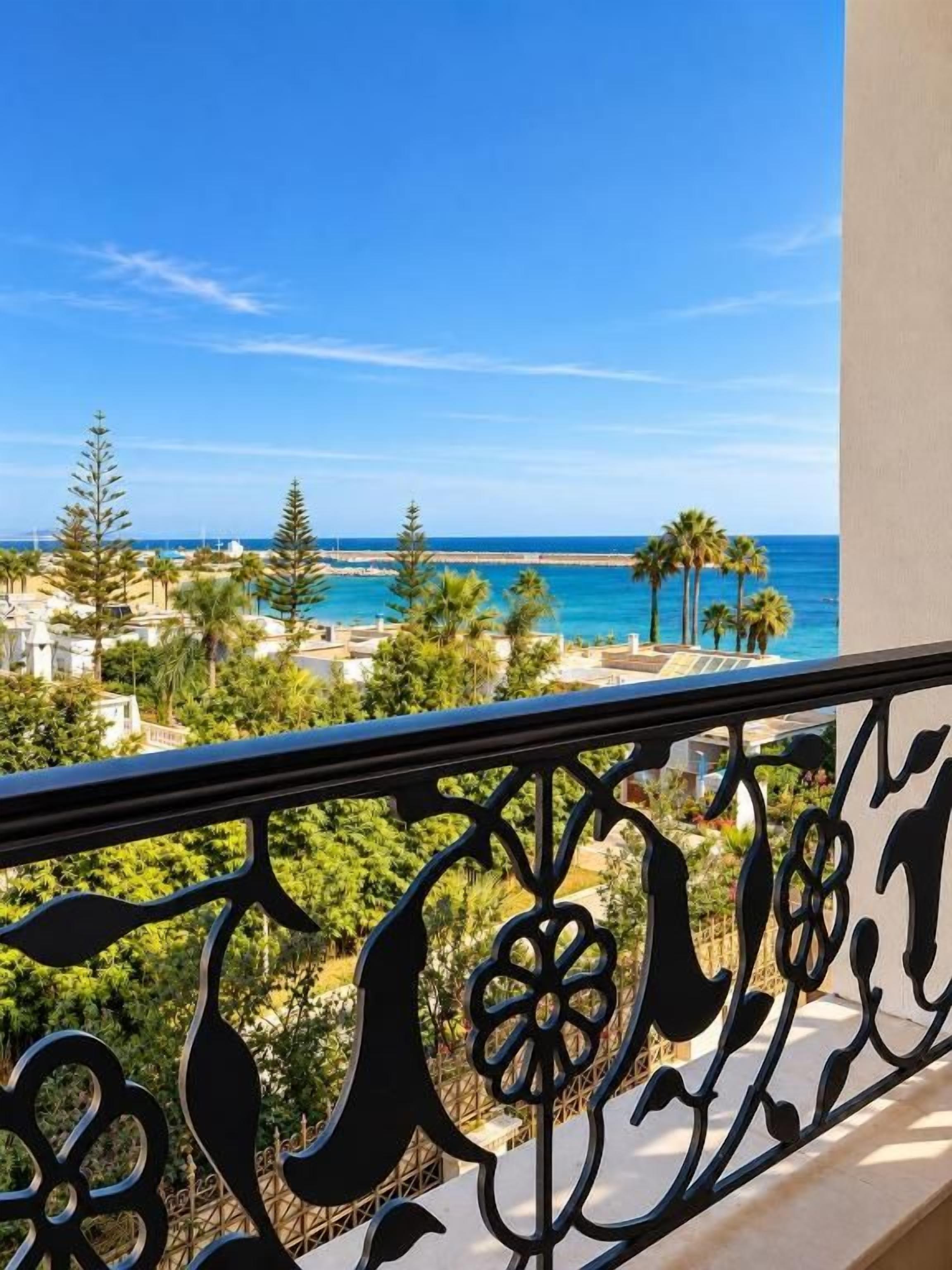 Un balcón con vista al mar, palmeras y cielo despejado.