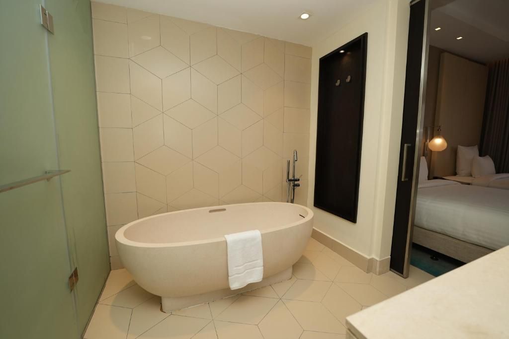 Un baño moderno con una bañera independiente, una cabina de ducha con paredes de vidrio y una cama visible en la habitación contigua.