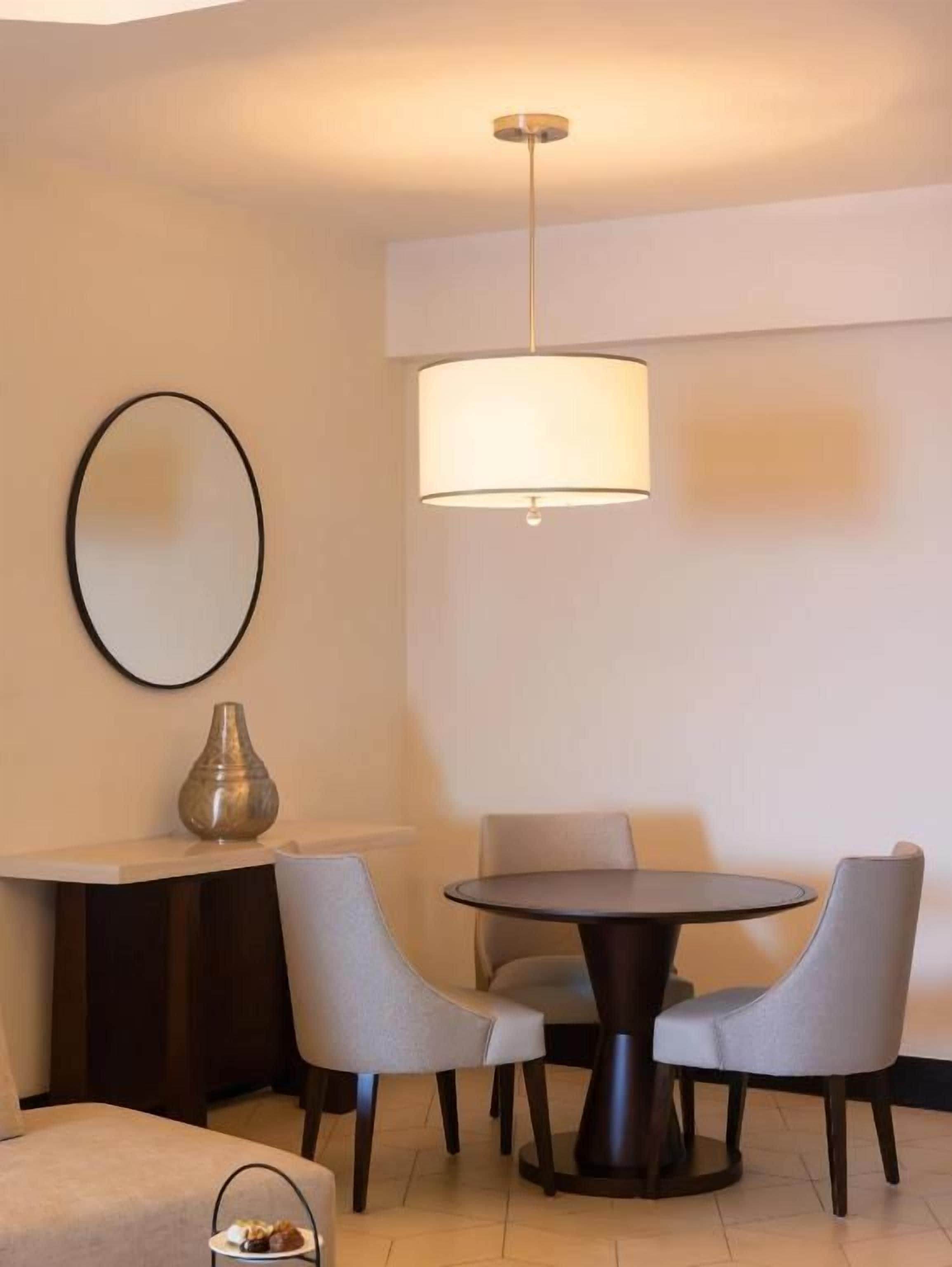 A dining area with a round table, four chairs, a vase, and a hanging lamp.