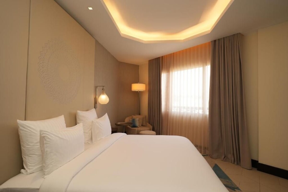 Una habitación de hotel con una cama grande, un escritorio, una silla y un ventanal con cortinas.