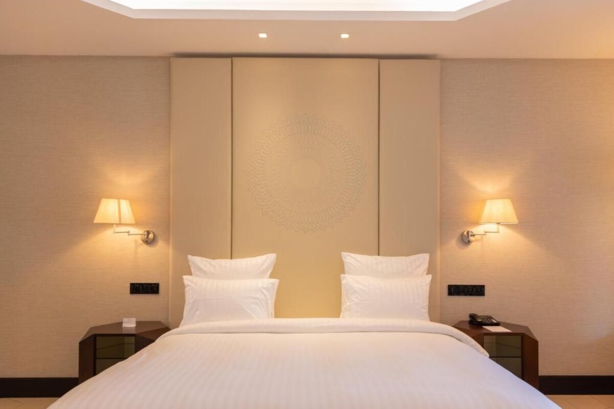 Una habitación de hotel con una cama grande, dos mesitas de noche y lámparas de pared.