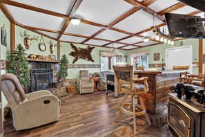 A rustic interior with wooden beams, a fireplace, leather recliners, and a bar area.