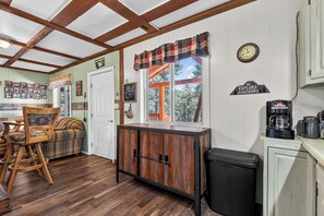 A rustic kitchen with wooden cabinetry, a dining area with a plaid sofa, and a window with a view of trees.