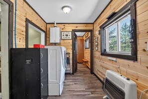 L’intérieur d’une cabane avec des murs en bois, un lave-linge, un radiateur et une fenêtre donnant sur un paysage agréable.