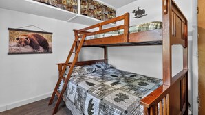 A bunk bed with a ladder, a quilt with animal patterns, a framed wildlife picture, and a shelf with animal-themed decor.