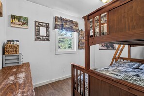 Une chambre avec un lit superposé en bois, un bureau, une fenêtre donnant sur la forêt et des éléments de décoration murale, notamment un miroir encadré et une image d’un orignal.