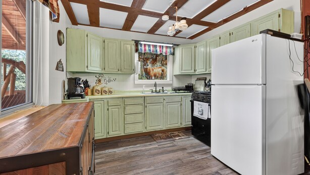 A kitchen with green cabinets, a white refrigerator, wooden beams, and a window with a view.