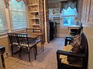 A dining area with a table and chairs, a kitchen area with a refrigerator and oven, and a window with curtains.