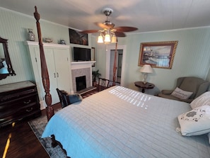 A bedroom with a four-poster bed, a fireplace, a television, and a ceiling fan.