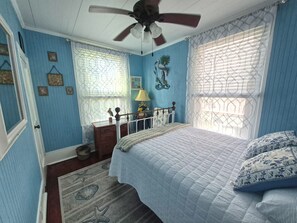 A bedroom with a bed, a nightstand, a dresser, a ceiling fan, and a window with patterned curtains.
