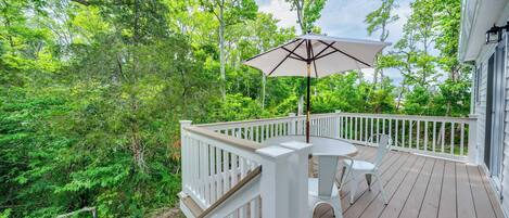A wooden deck with white railings, a table with two chairs, and an umbrella.