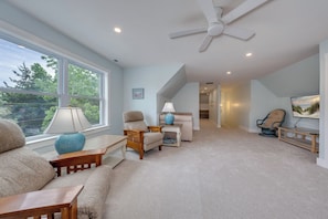 A spacious living room with a ceiling fan, large windows, a sofa, a coffee table, and a TV. - Salt & Cedar House -large gathering spaces, 5 min to stone harbor, Bar&Game Room (Middle Township)