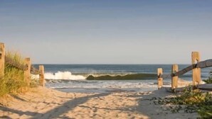 Een strandpad dat naar de oceaan leidt, met houten afscheidingen en begroeiing.