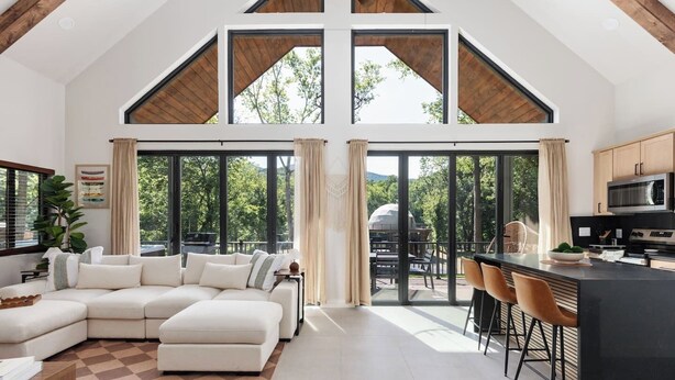 A spacious living area with a large L-shaped sofa, a kitchen with modern appliances, and large windows offering a view of the outdoors. - River Run - Riverfront+Pickleball+Hot Tub+Sauna (Shenandoah)