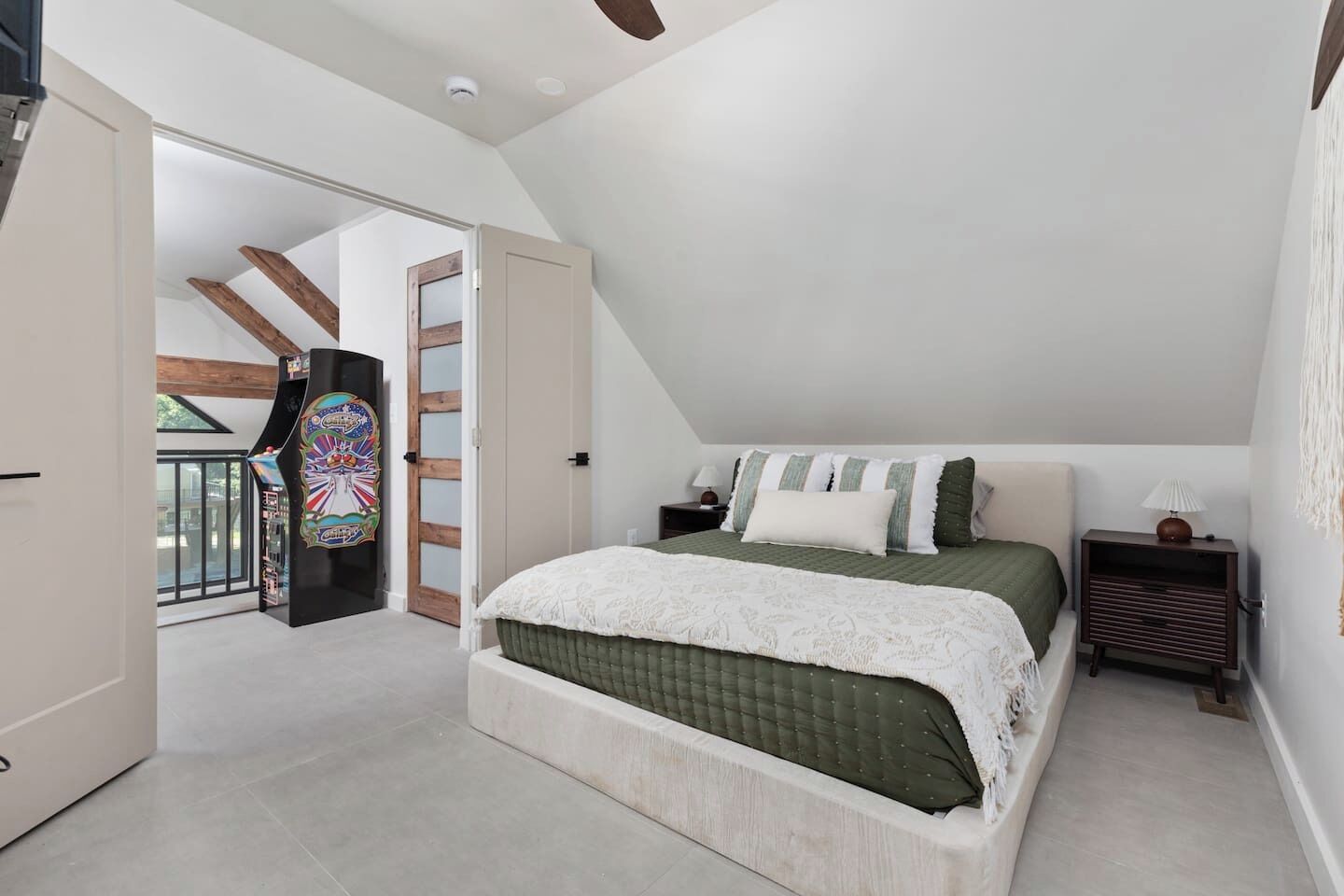 A bedroom with a bed, bedside tables, a lamp, a door, and a view of the outside.