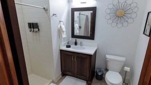 Baño con ducha, inodoro, lavamanos y espejo.