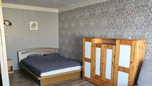 Een kamer met een bed, een houten kastje, een klein tafeltje en een behang met patroon.