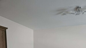 Een kamer met twee zwarte stoelen, een houten kast en een wit plafond met een lamp.
