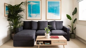 A living room with a sectional sofa, a coffee table, two framed artworks, and potted plants. - Colourful house 2 bedroom Apt - Notting Hill (Greater London)