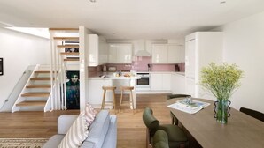 A modern kitchen with white cabinets, a dining area with a wooden table and chairs, a staircase leading to an upper level, and a living room with a sofa and a rug. - The Iconic Portobello Mews House (Greater London)