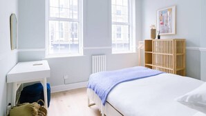 Ein Schlafzimmer mit zwei Fenstern, einem Bett mit blauer Decke, einem Holzschrank und einer Heizung.
