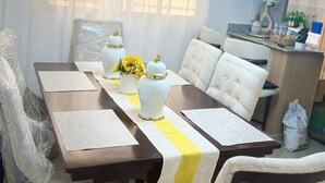 Een eetgedeelte met een tafel gedekt voor vier personen, een kroonluchter en een keuken op de achtergrond.